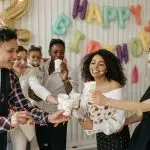 A diverse group of friends celebrating a birthday indoors with party hats and balloons.