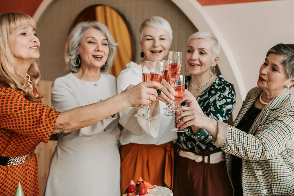 A festive scene showing how do Germans celebrate birthdays, with a group of people raising glasses of sparkling wine in a toast. The table in front of them features a cake topped with strawberries, surrounded by a warmly decorated room that highlights the joyful celebration.